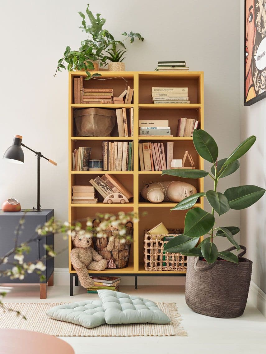 Żółty regał z książkami i zabawkami w kąciku dziecięcym w salonie